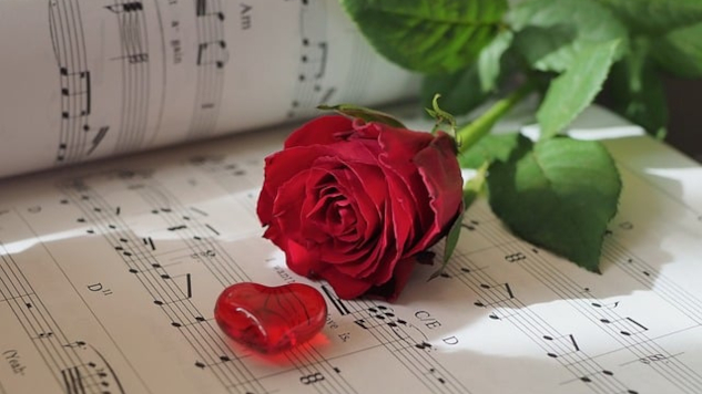 a drawing of a heart with a red rose in full bloom laying on a sheet of music